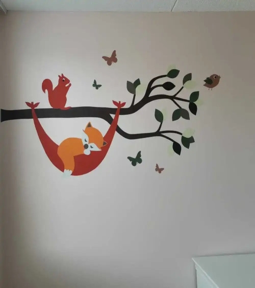 Muursticker babykamer tak met vosje in hangmat in natuurlijke groentinten.