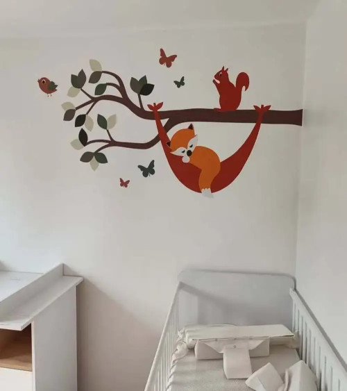 Muursticker babykamer tak met vosje in hangmat in natuurlijke groentinten.