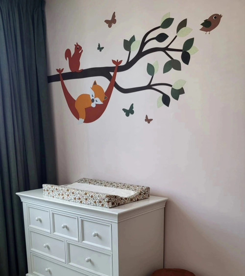 Muursticker babykamer tak met vosje in hangmat in natuurlijke groentinten.