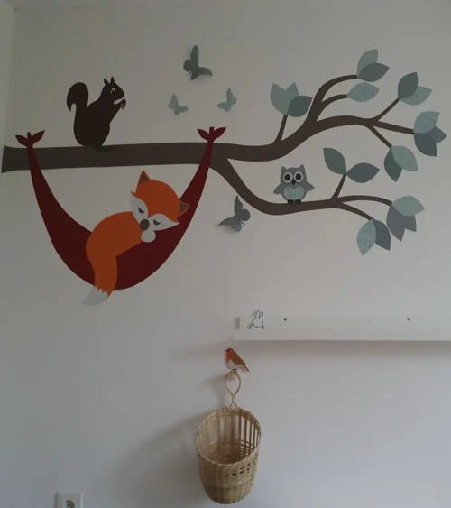Muursticker babykamer tak met vosje in hangmat in natuurlijke groentinten.
