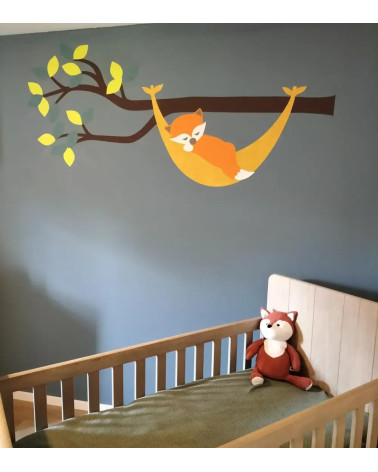 Muursticker babykamer tak in natuurlijke groentinten met een oranje vosje in een okergele hangmat.