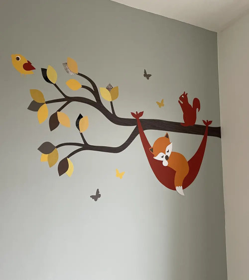 Muursticker babykamer tak met vosje in hangmat in natuurlijke groentinten.