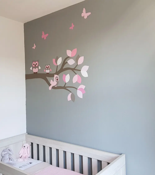 Behangsticker roze sierlijke uilentak op een grijze muur in een meisjesbabykamer.
