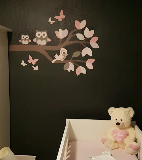 Muursticker tak met roze uilen op een zwarte muur in de meisjes babykamer.