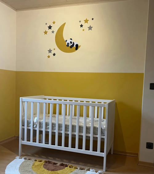 Een okergele babykamer met een behangsticker met een slapende pandabeer op een maan.
