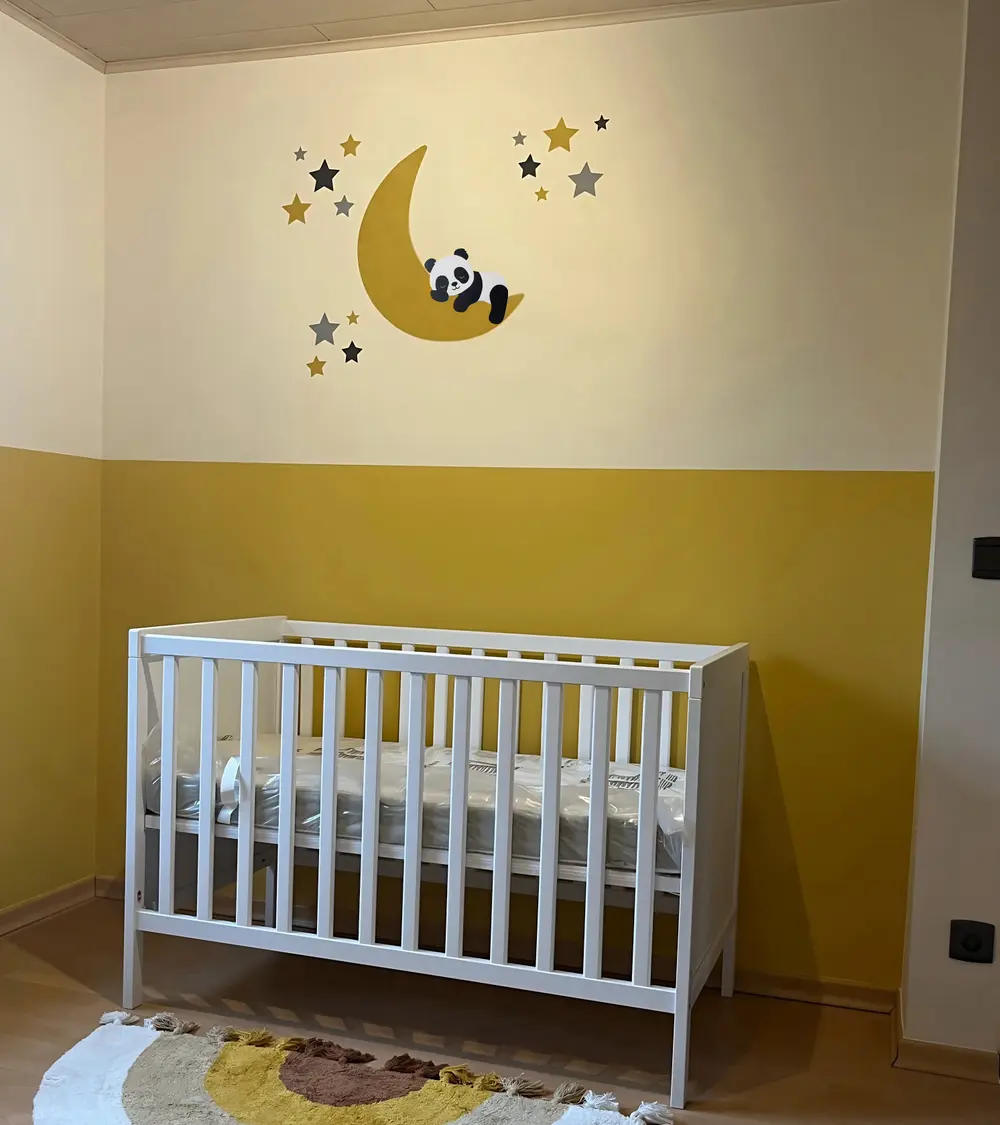 Een okergele babykamer met een behangsticker met een slapende pandabeer op een maan.