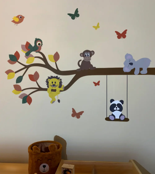 Behangsticker van een tak met dieren boven de commode in de babykamer in vrolijke kleuren groen, okergeel en rood.