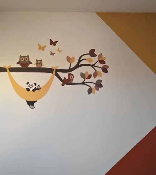 Babykamer met muurvlakken en een muurdecoratie met uiltjes en panda in hangmat.