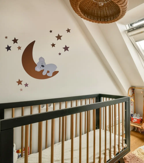 Een behangsticker viir de babykamer met een slapend koalabeertje op een roestbruine maan met sterren.