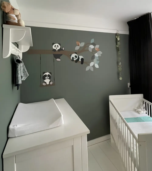 Behangsticker met pandabeertjes op een tak in een donker groene babykamer.