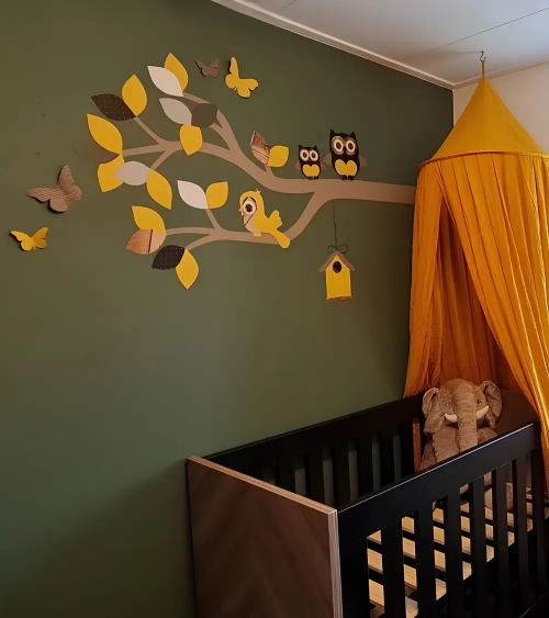 Behangsticker sierlijke uilentak okergeel op een donkergroene muur in de babykamer.