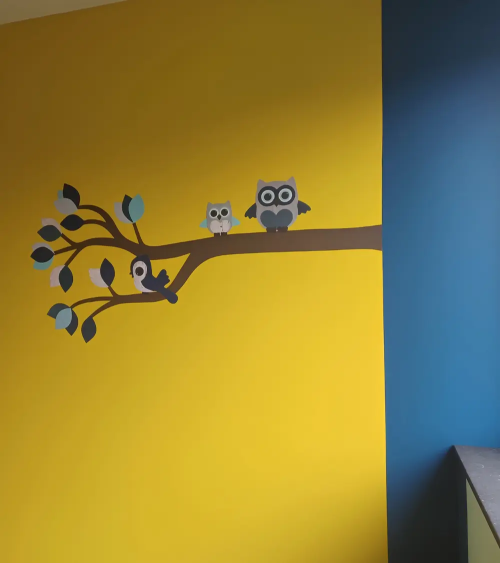 Sierlijke uilentak licht- en donkerblauw in een okergele jongensbabykamer.