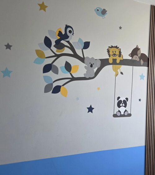 Een behangsticker van een blauwe en okergele tak met lieve diertjes, zoals een leeuwtje, vosje, panda, koala en vogels.