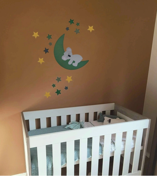 Behangsticker van een slapende koala op een donkergroene maan met sterren op een bruine wand in de babykamer.