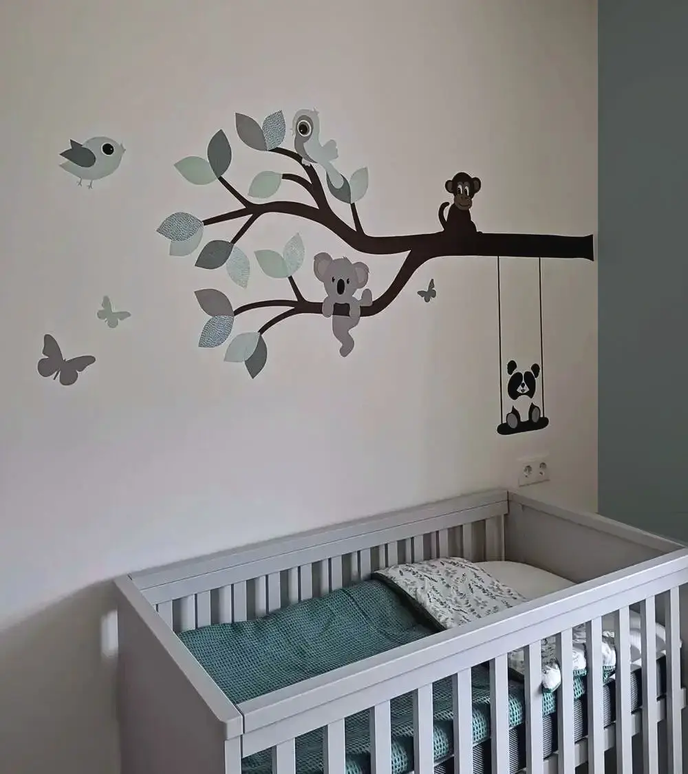 Behangsticker van een tak met vrolijke dieren in mintgroen en oudgroen in een lichte neutrale babykamer.