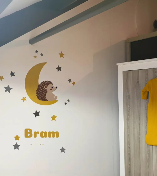 Egel behangsticker op een okergele maan met sterren en naamsticker in een neutrale babykamer.