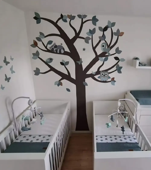 Groene tweeling babykamer met oudgroene behangboom met bosdieren, zoals een uil, wasbeer en vogels.