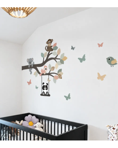 Een wanddecoratie van een tak met vrolijke dieren en schommel boven het babybedje in oudroze en oudgroen.