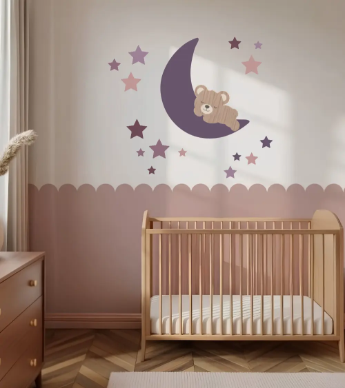 Een behangdecoratie voor de kinderkamer van een slapende teddybeer op een maan en sterren in paars en roze.