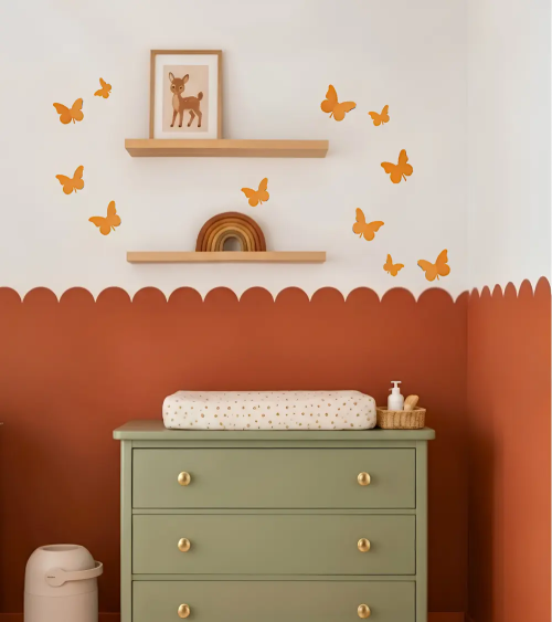 Okergele 3D vlinders als muurdecoratie boven de commode in een terracotta babykamer.