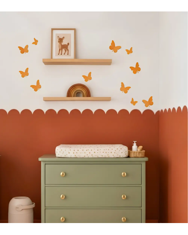 Okergele 3D vlinders als muurdecoratie boven de commode in een terracotta babykamer.